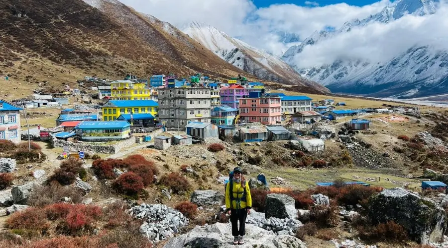 A trekker posing in front of Kyanjin Gompa with the view of mountains in the background