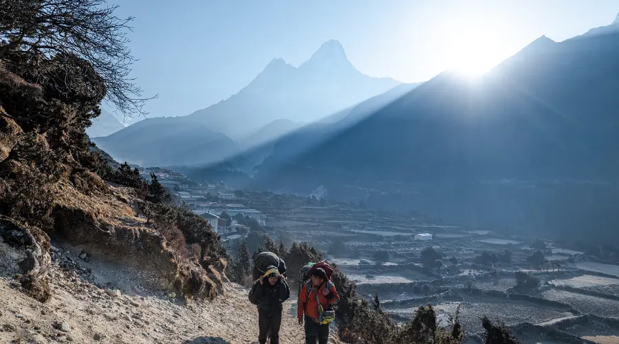 Trekker and porter walking on the EBC trail with the view of Ama Dablam in the background