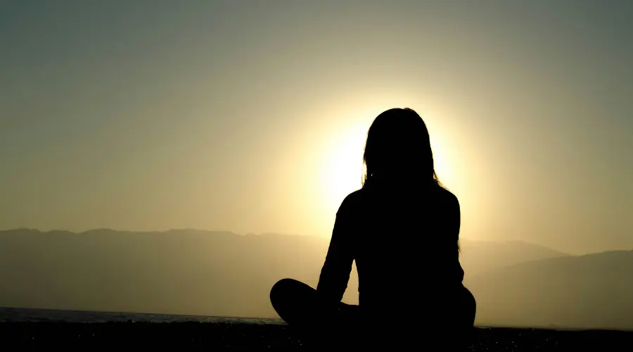 A person meditating with the sunrise in the background