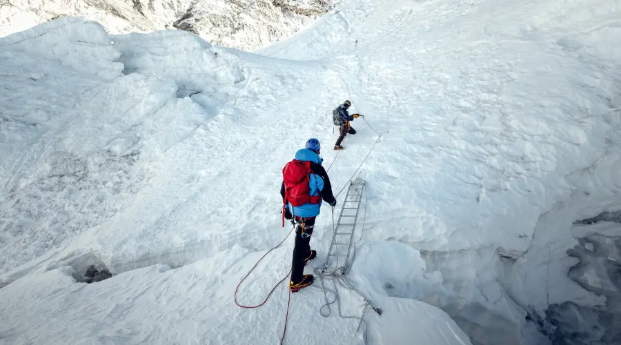 Mountaineers crossing a crevasse using a ladder and a rope